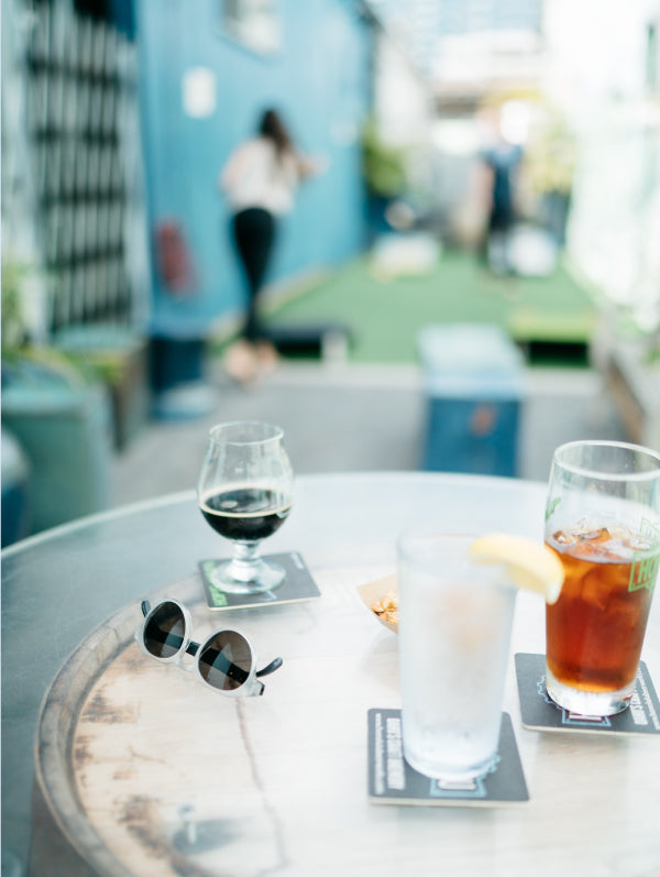 A pair of Cooper MagLock sunglasses sit on a table with pints of cold beers while people play games in the background