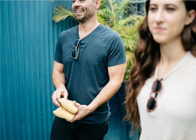 A guy and woman keep their MagLock Sunglasses on their shirt while playing cornhole